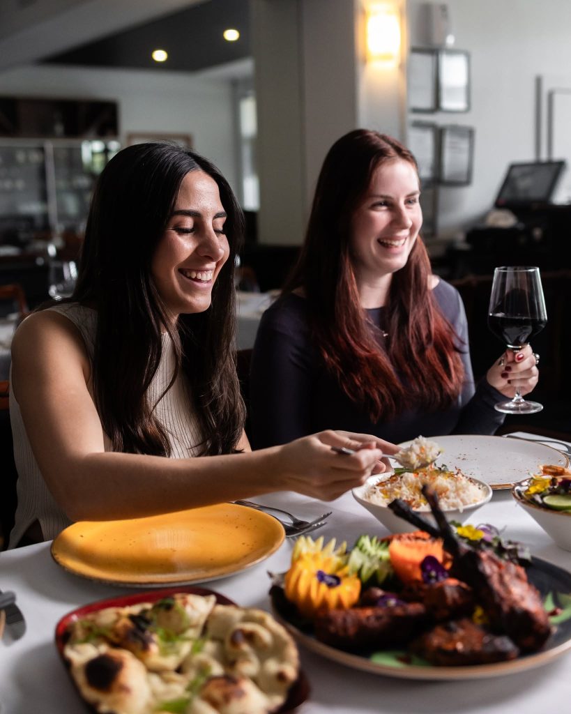 Friends sharing tandoori lamb chops, naan and rice with red wine at a family restaurant in Melbourne