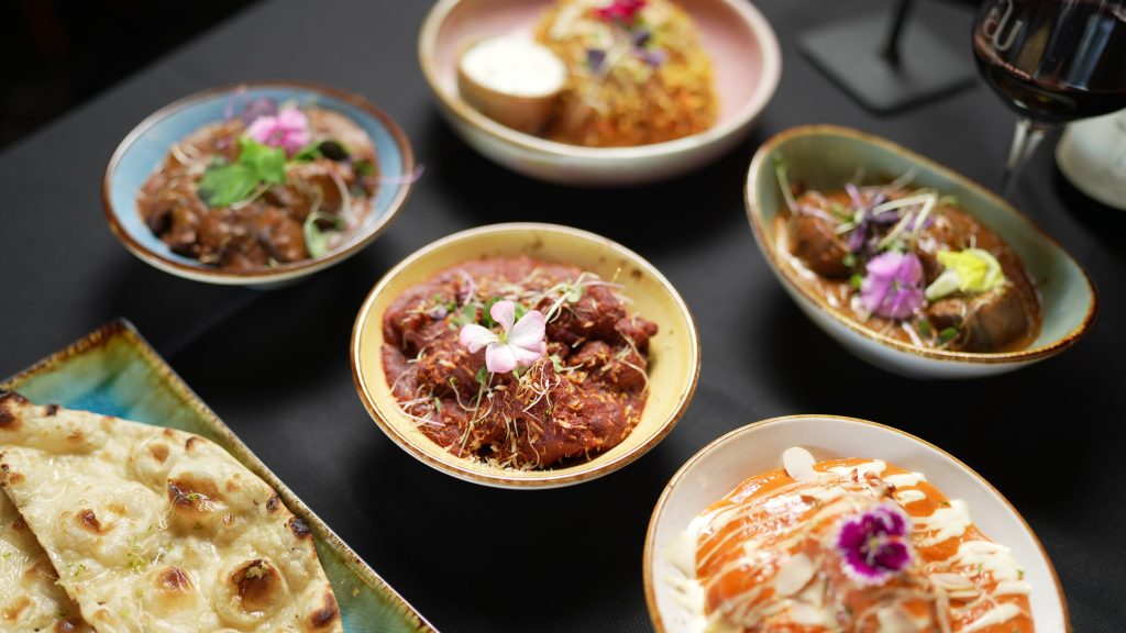 Indian restaurant dishes featuring naan, curries, kebabs and beautifully garnished plates served on a table.