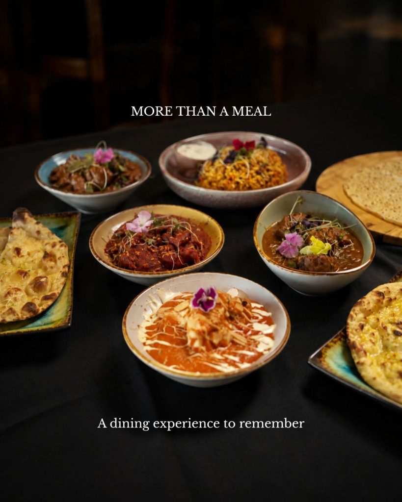 Waadiya Indian restaurant spread featuring biryani, rich curries, butter chicken, naan bread and papad, garnished with fresh herbs and edible flowers on a dining table.